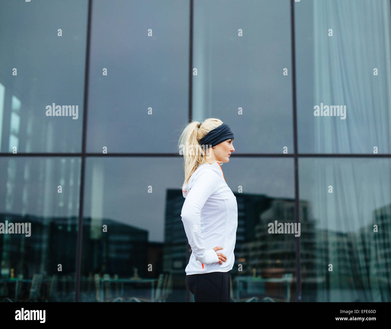 Seitlicher Blick auf eine sportliche junge Frau bereit für ihre outdoor-Training-Session. Fitness-Frau stehend im Freien mit Hände auf den Hüften. Stockfoto