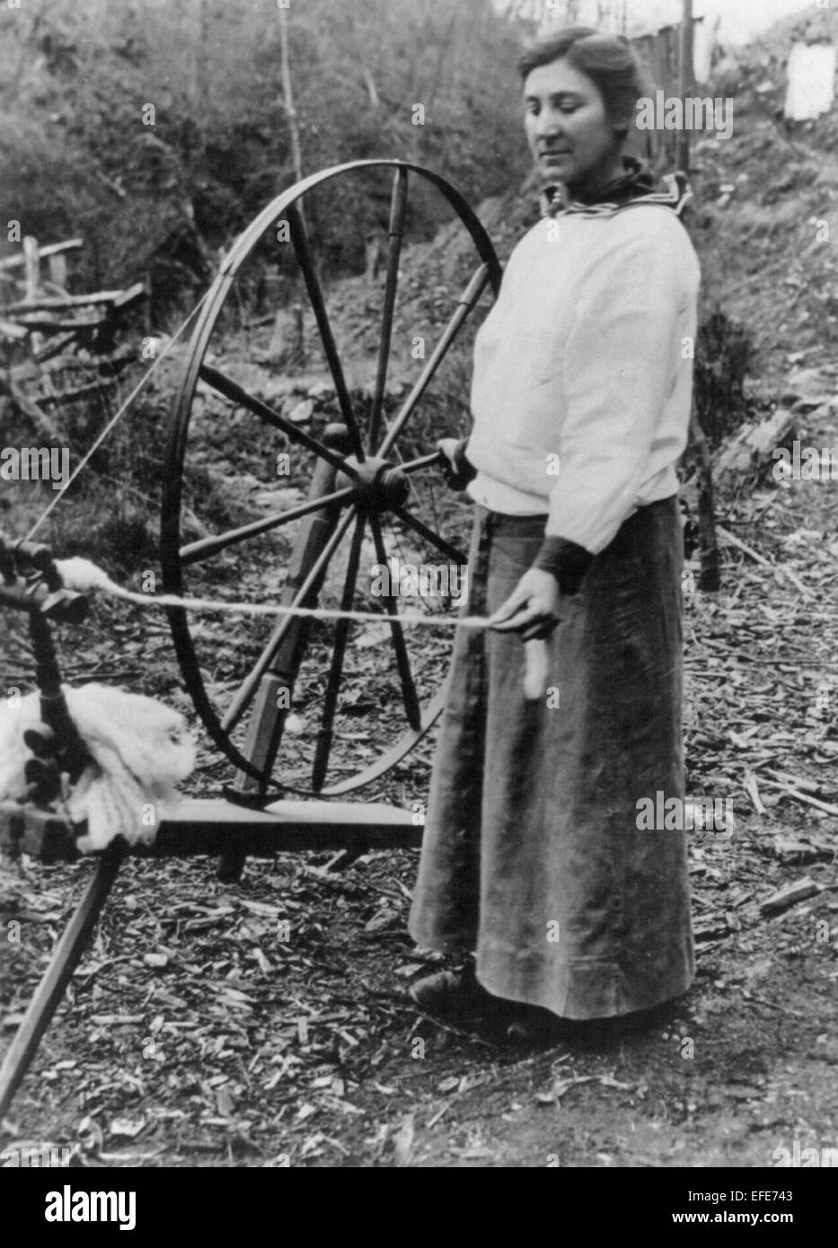 "Großmutters Spinnrad reduziert die hohen Lebenshaltungskosten" Frau stehend, im Freien, mit Spinnrad, ca. 1920 Stockfoto