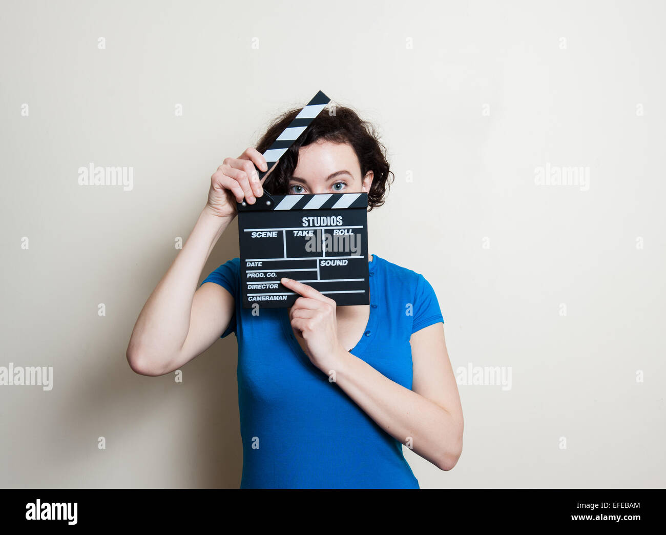 Mädchen im blauen T-shirt mit lachenden Augen zeigen Film Klöppel auf weißem Hintergrund Stockfoto