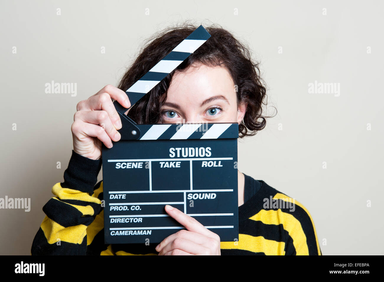 Mädchen in gelbes T-shirt mit lachenden Augen zeigen Film Klöppel auf weißem Hintergrund Stockfoto