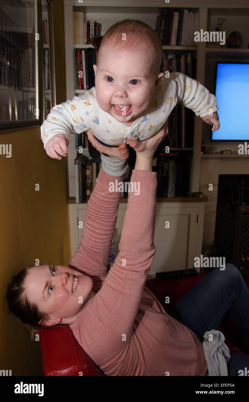 Eine Mutter Anhebung ihrer glückliches fünf Monate altes Baby über den Kopf fliegen zu imitieren. Stockfoto