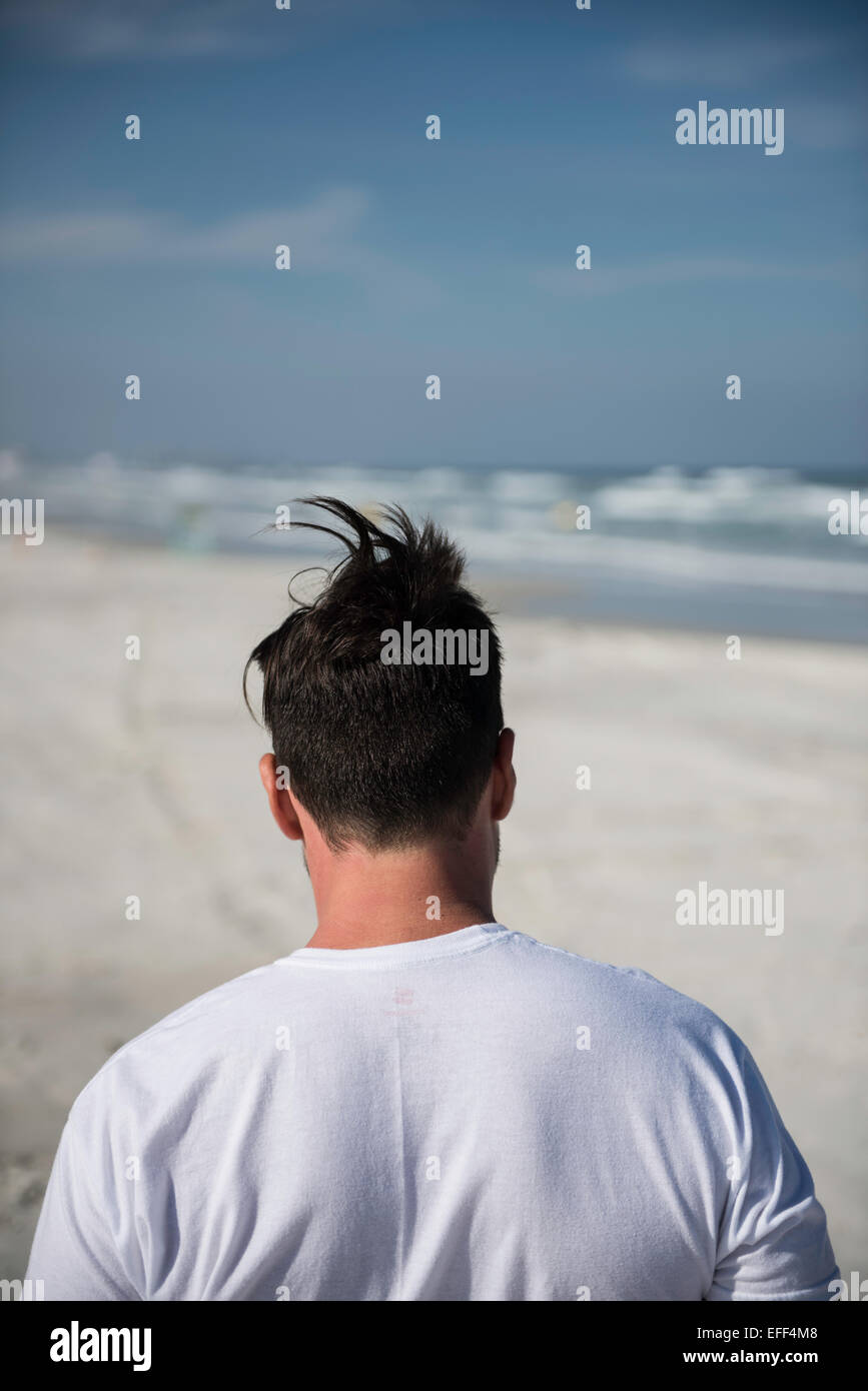 Nahaufnahme von Kopf, Nacken und Schultern eines Mannes gesehen von hinten zu Fuß am Strand mit Wind Haar zu einem humorvollen Stockfoto