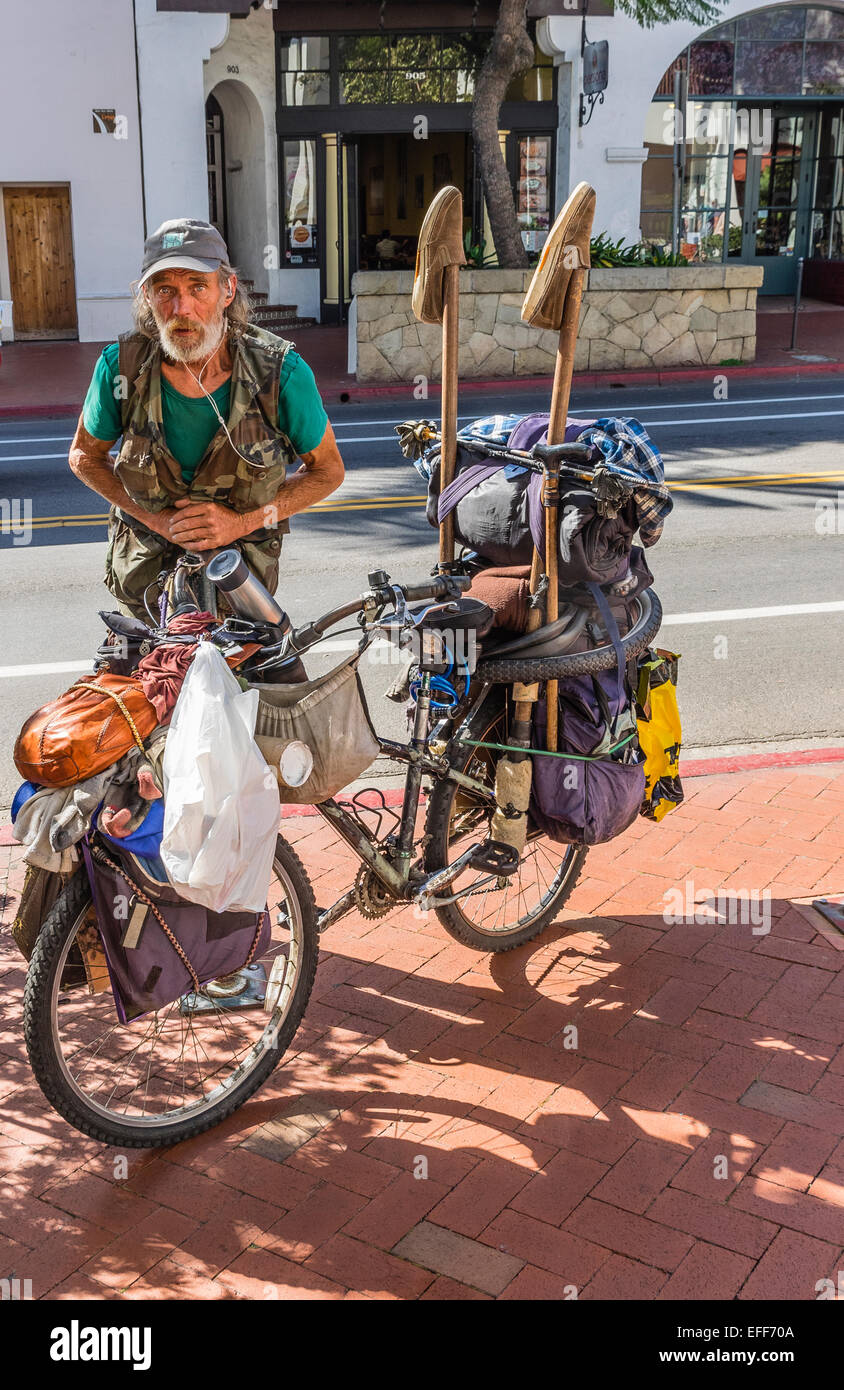 Eine Obdachlose Senioren zeichnet sich durch sein Fahrrad beladen mit seiner weltlichen Zugehörigkeit und tragen Ohrhörer zum hören von Musik. Stockfoto