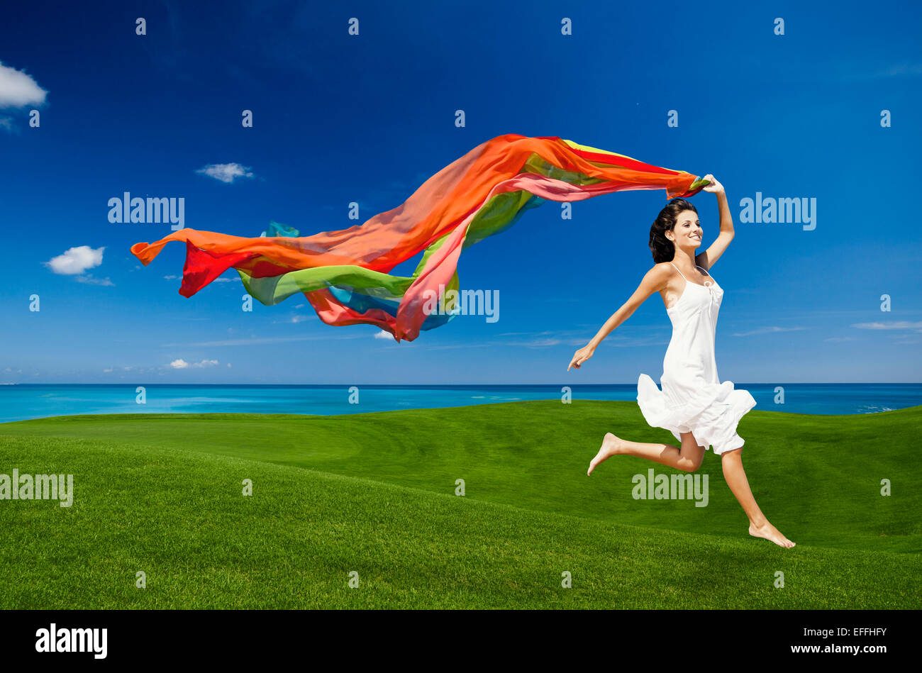 Schöne Frau springen auf einer grünen Wiese mit farbigen Geweben Stockfoto