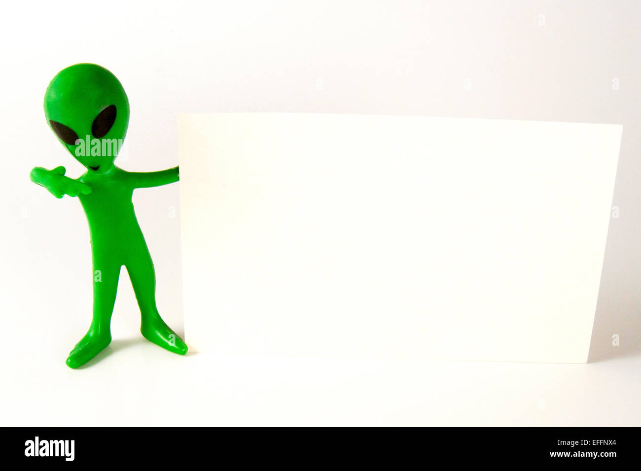 Kleinen grünen Alien anrufen mich Geste hielt eine leere Notiz-Karte Stockfoto