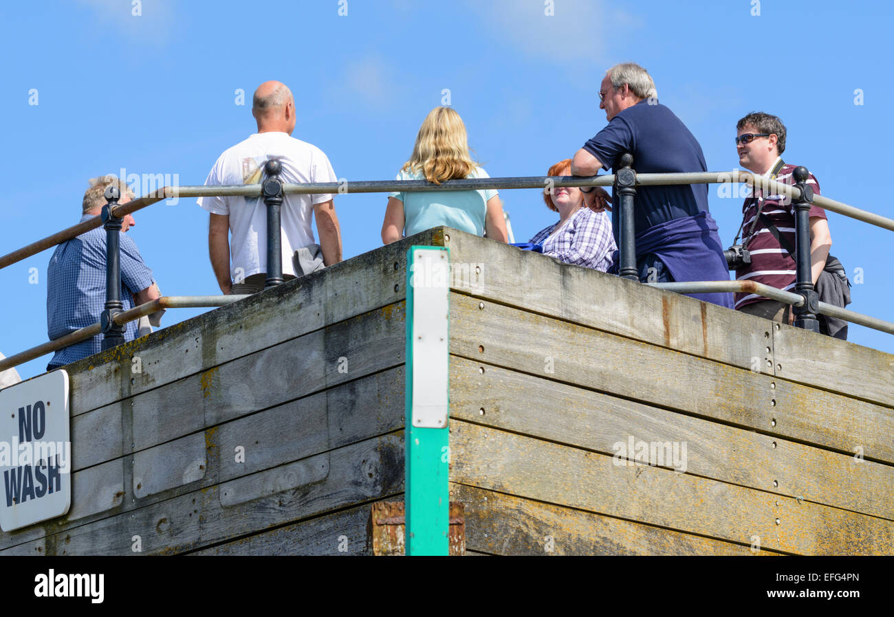 Mehrere Personen stehend reden auf einer Mole mit blauen Himmel oben. Stockfoto