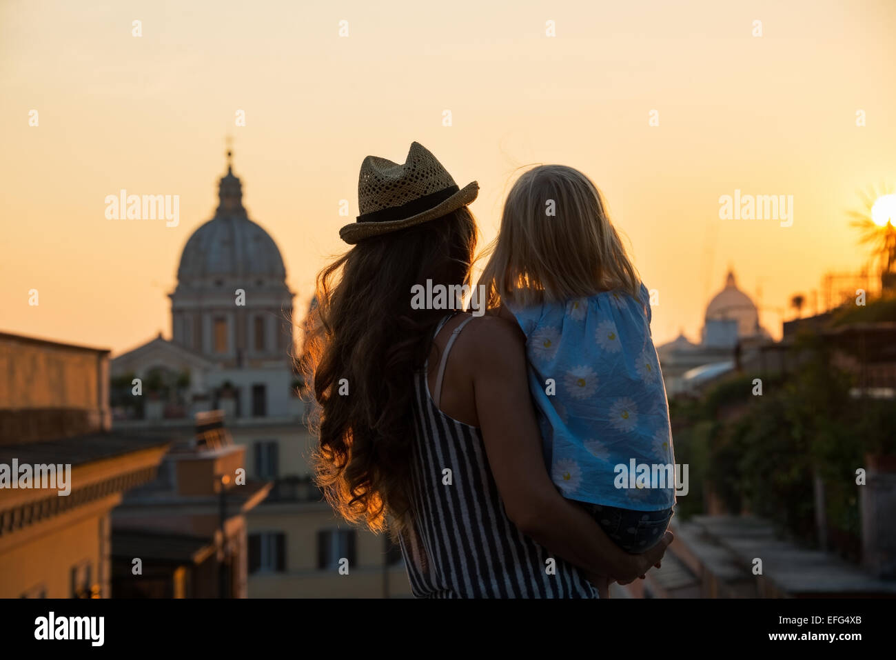 Silhouette von Mutter und Baby Mädchen auf der Suche auf den Dächern von Rom am Sonnenuntergang. Rückansicht Stockfoto