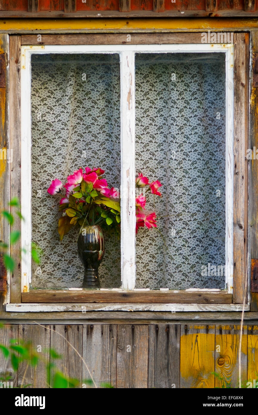 Fenster einer alten hölzernen Häuschen mit roten Rosen in einer Vase. Pommern, Polen. Stockfoto