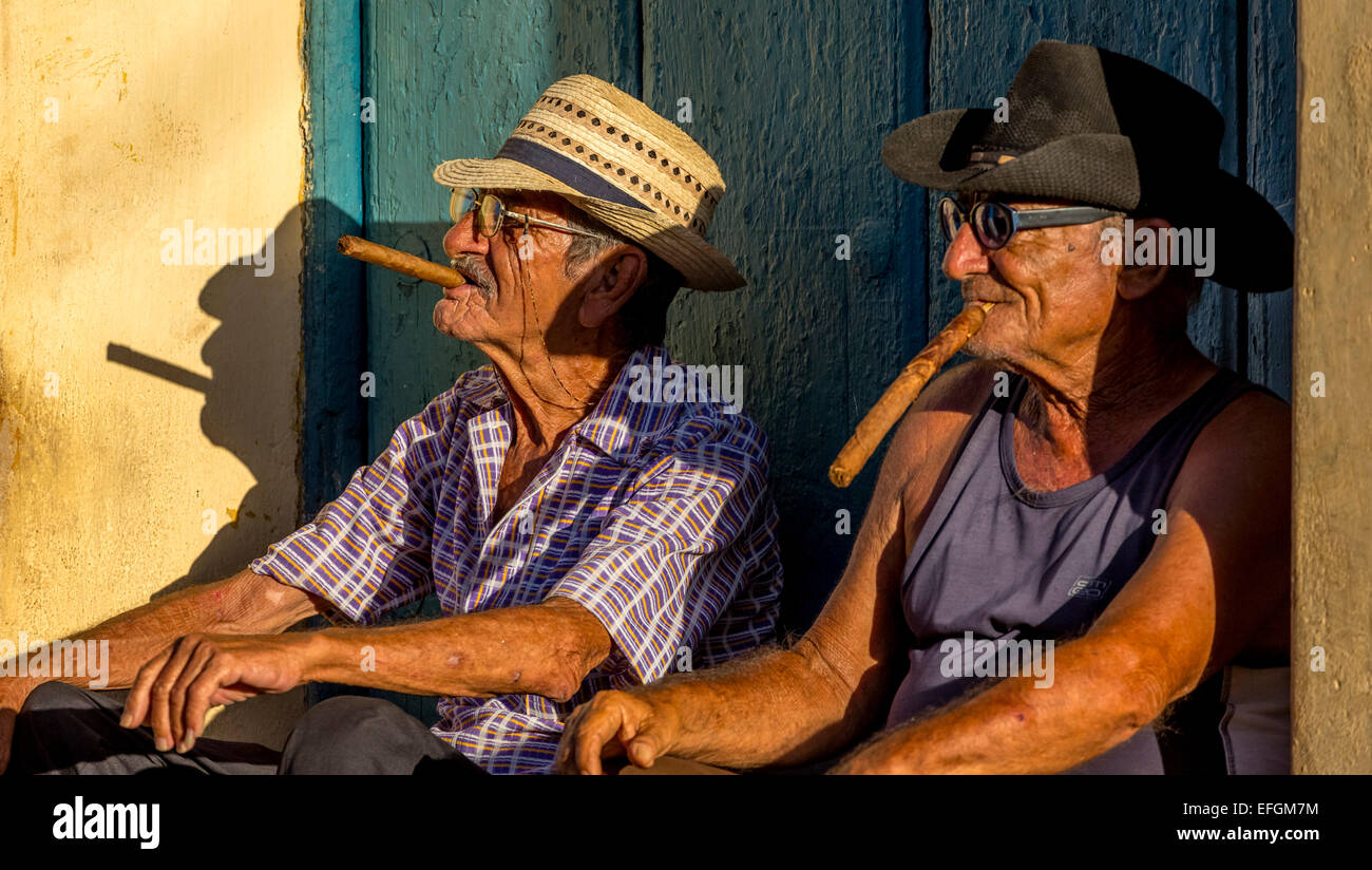 Zwei ältere Kubaner sitzen auf einer Haustür im Abendlicht, rauchen Zigarren, Trinidad, Provinz Sancti Spiritus, Kuba Stockfoto