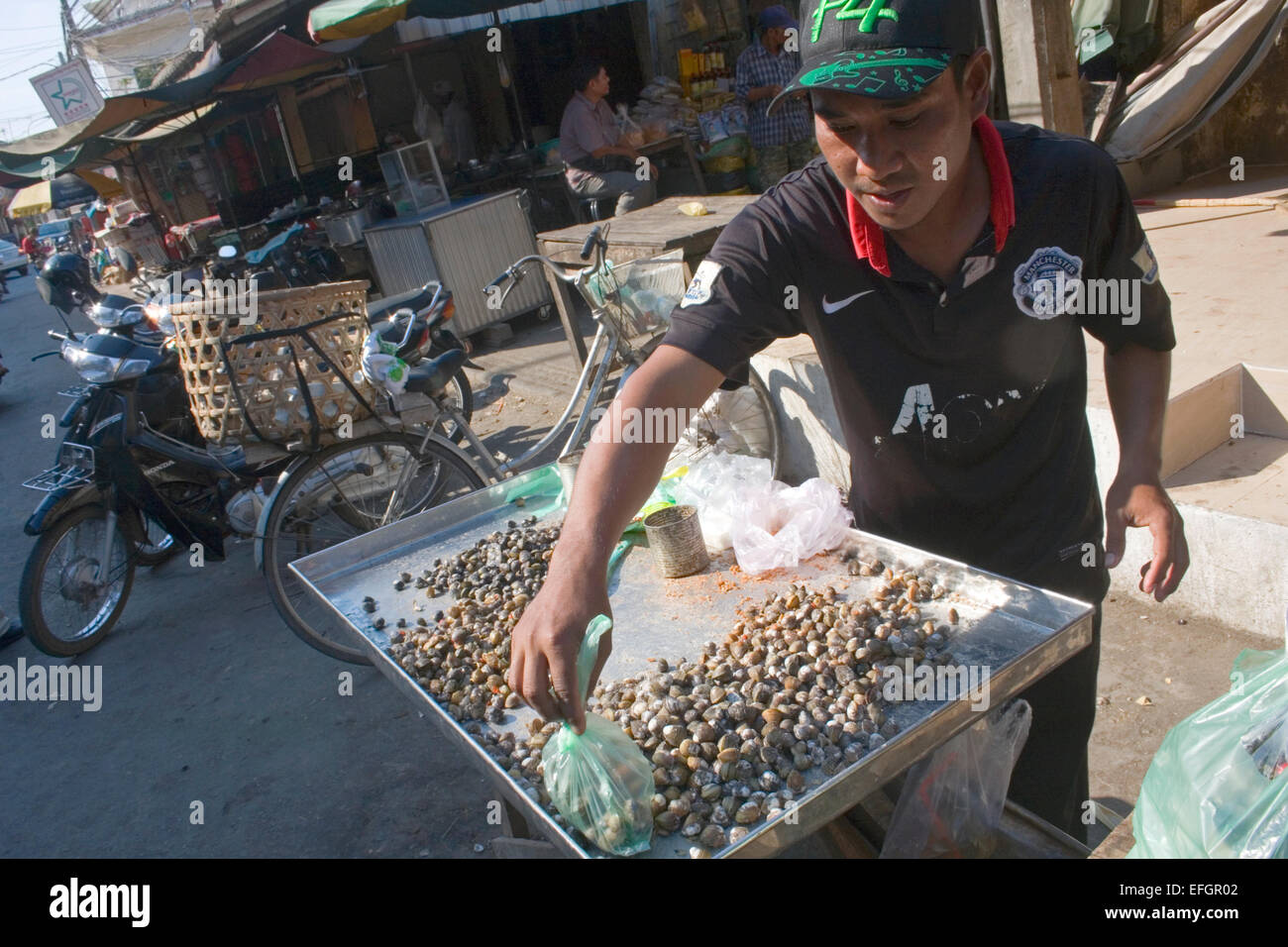 Einem Mann Straßenhändler verkauft Schnecken als Straße Nahrung auf eine Stadt Straße in Kampong Cham, Kambodscha. Stockfoto