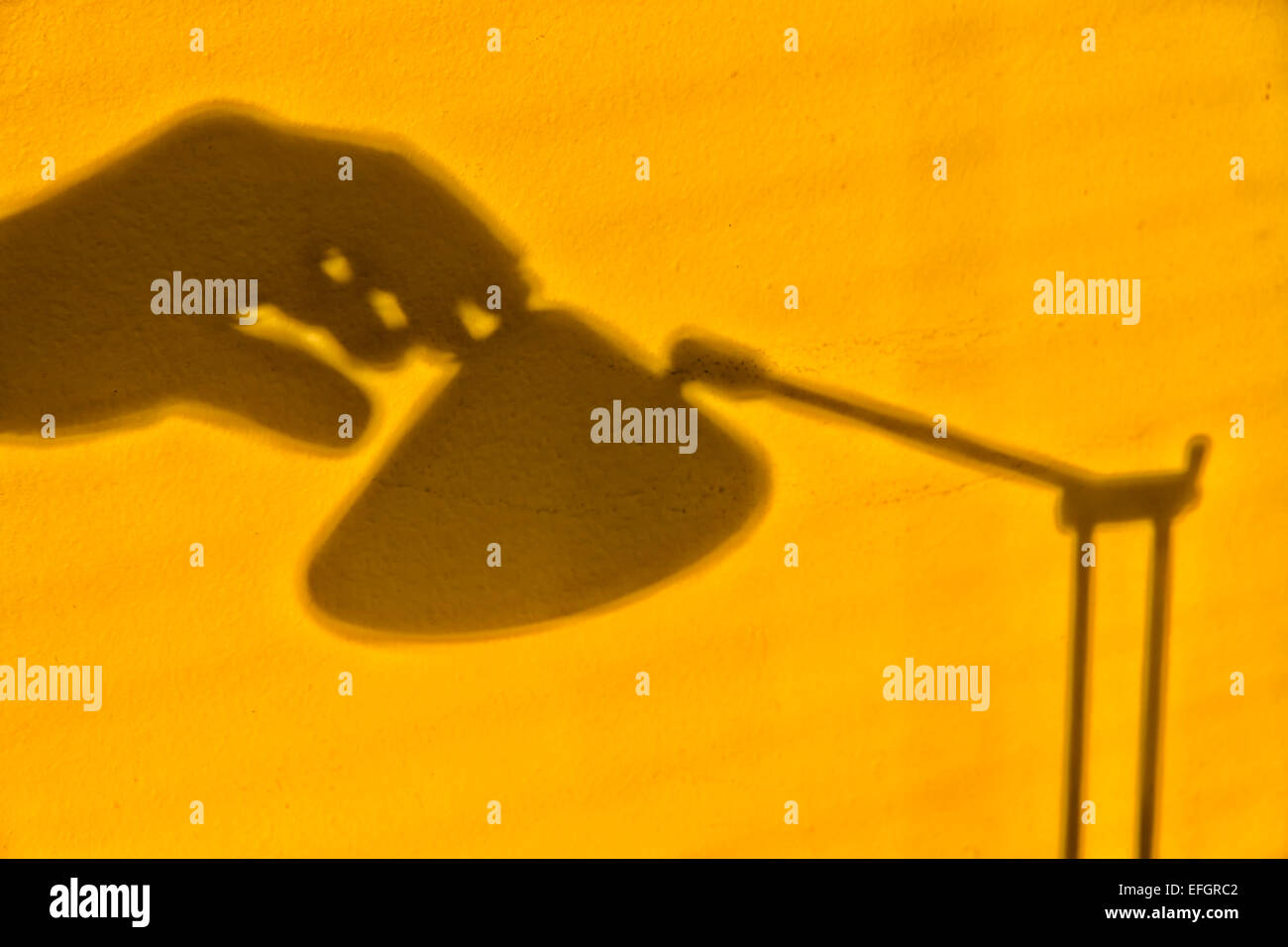 Unheimliches Bild einer gelb lackierten Wand mit Schatten einer Hand, die nach dem Schalter einer Tischleuchte aus Metall streckt Stockfoto
