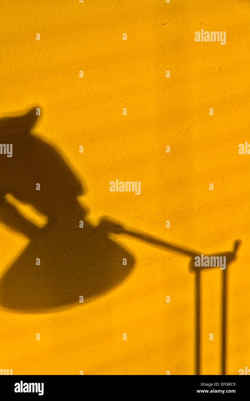 Unheimliches Bild einer gelb lackierten Wand mit Schatten einer Hand, die nach dem Schalter einer Tischleuchte aus Metall streckt Stockfoto