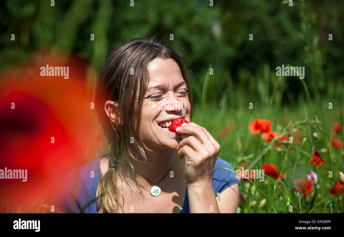 Junge Frau sitzt in einem blühenden Mohn-Feld eine Erdbeere essen Stockfoto