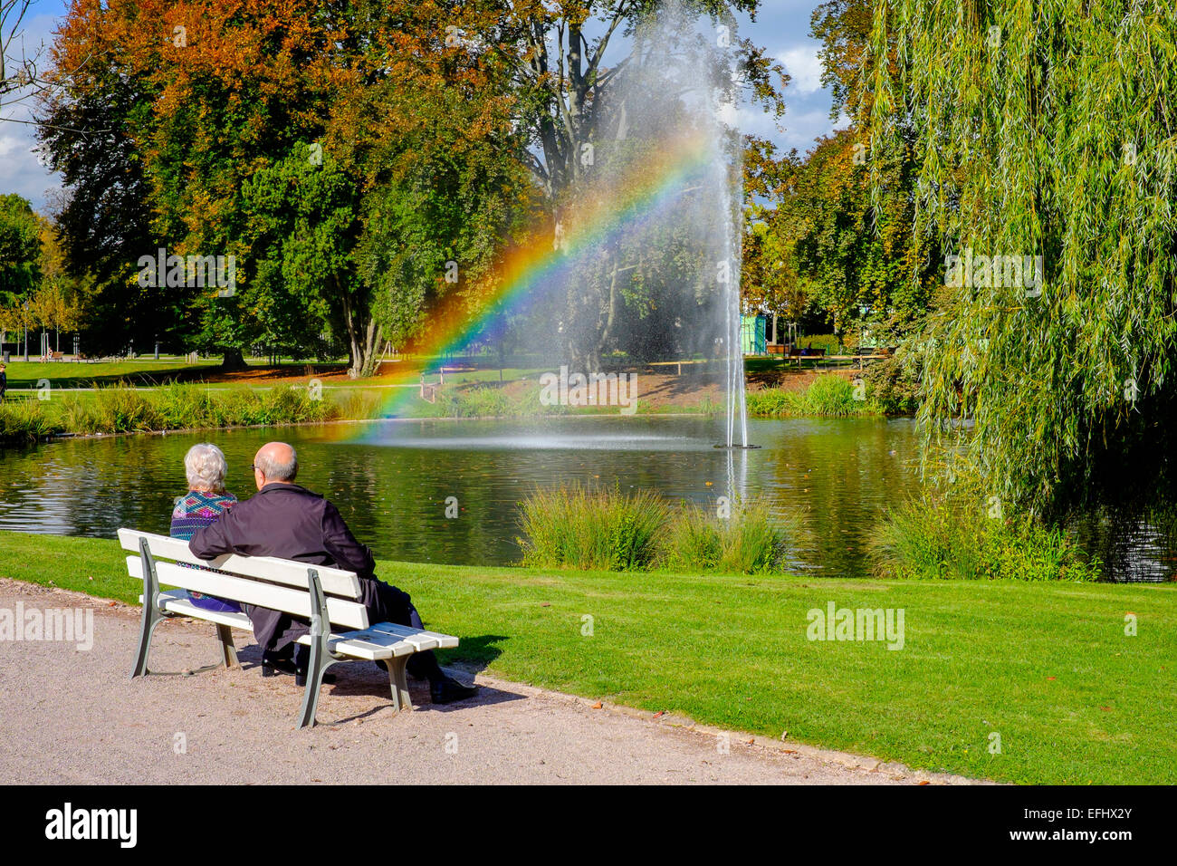 Ältere Paare auf der Werkbank, Wasserstrahl mit Regenbogen, Parc de l'Orangerie Park, Straßburg, Elsass, Frankreich, Europa Stockfoto