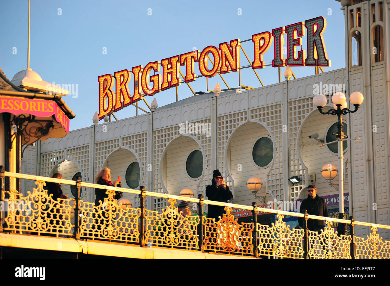 Touristen stehen an Deck der Brighton Pier bei Sonnenuntergang. Stockfoto