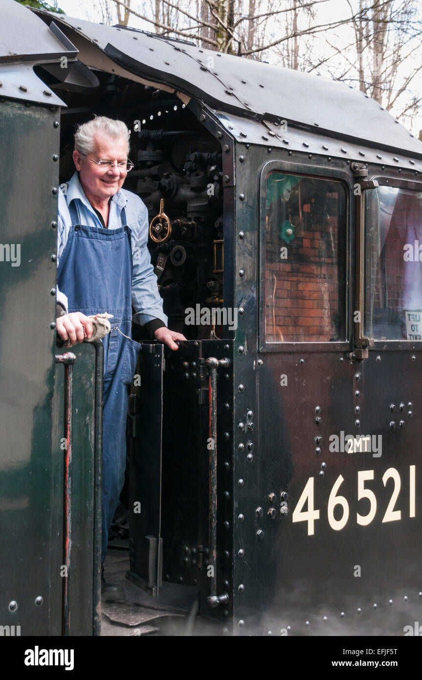 Der Zugfahrer steht und lächelt in der Fahrerkabine einer Dampflok, die eine Reiseszene nachstellt, die man in den 1940er, 1950er und 1960er Jahren häufig gesehen hat Stockfoto