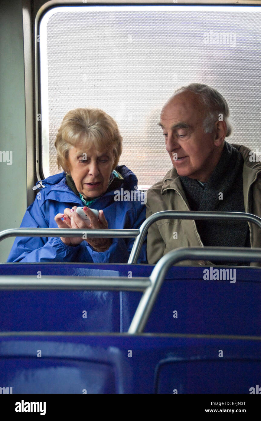 Vertikale Porträt eines älteren Paares sitzen zusammen in einem Bus mit einem Smartphone. Stockfoto