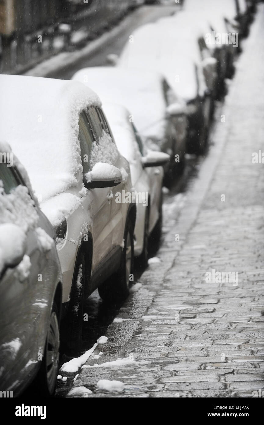 Städtisches Motiv mit parkenden Autos in einer Reihe mit Schnee bedeckt, während eines Schneefalls Stockfoto