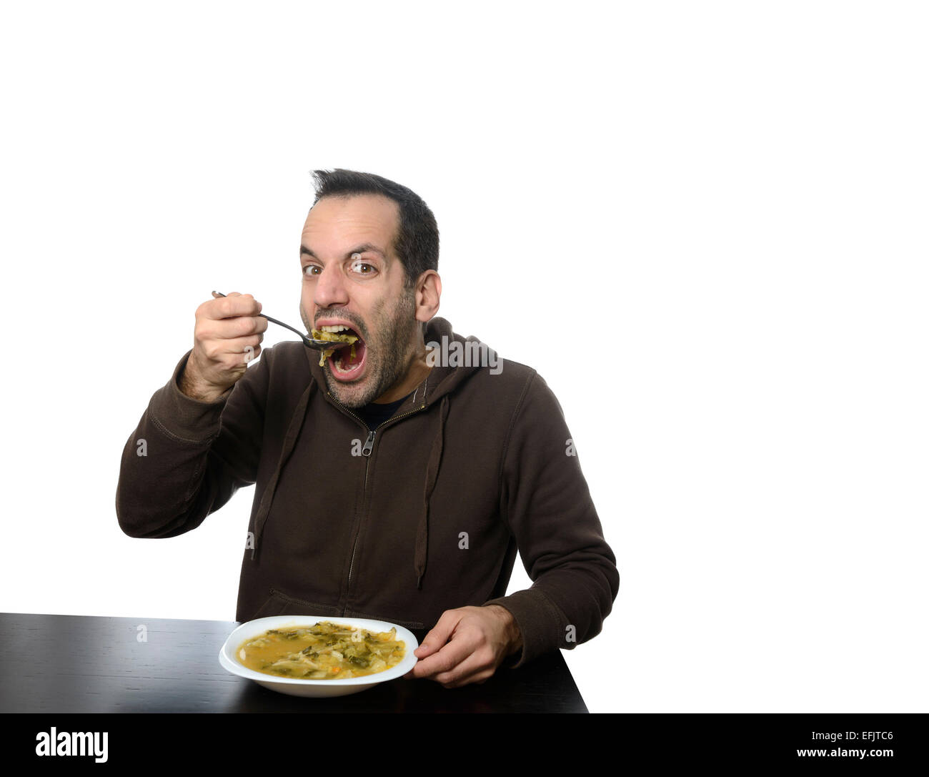 Junger Mann Essen Gemüsesuppe mit weit geöffnetem Mund Stockfoto