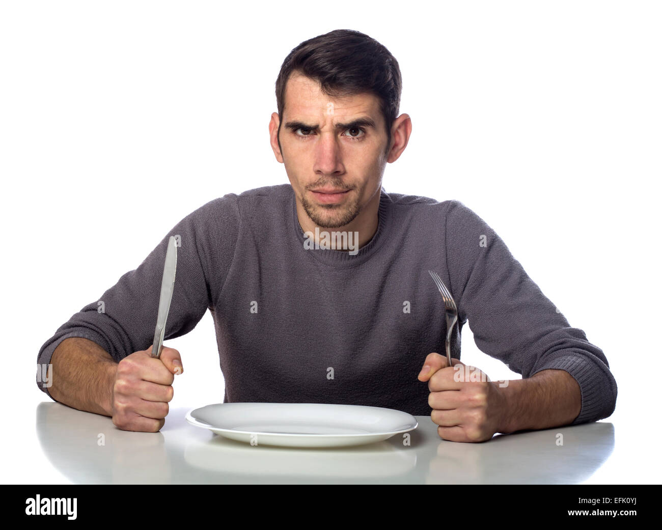 Mann am Tisch mit Gabel und Messer angehoben. Hungerstreik isoliert auf weißem Hintergrund Stockfoto