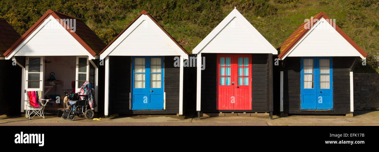 Rollstuhl und farbenfrohe Strandhütten mit blauen und roten Türen in einer Zeile traditionellen englischen Struktur und Obdach panorama Stockfoto