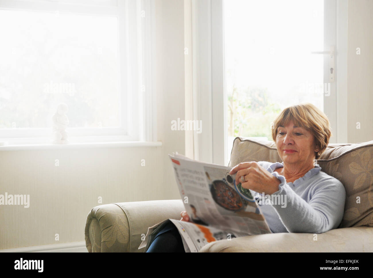 Ältere Frau im Sessel lesen Magazin Stockfoto