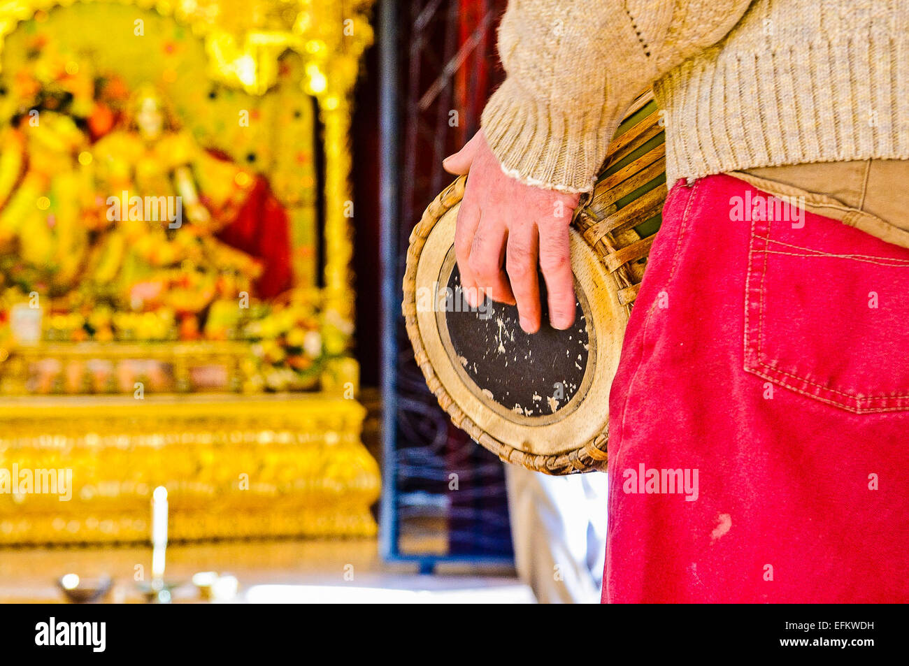 Ein Hare-Krishna-Anhänger spielt eine Mrdanga Trommel vor einem Altar im Tempel Raum. Stockfoto
