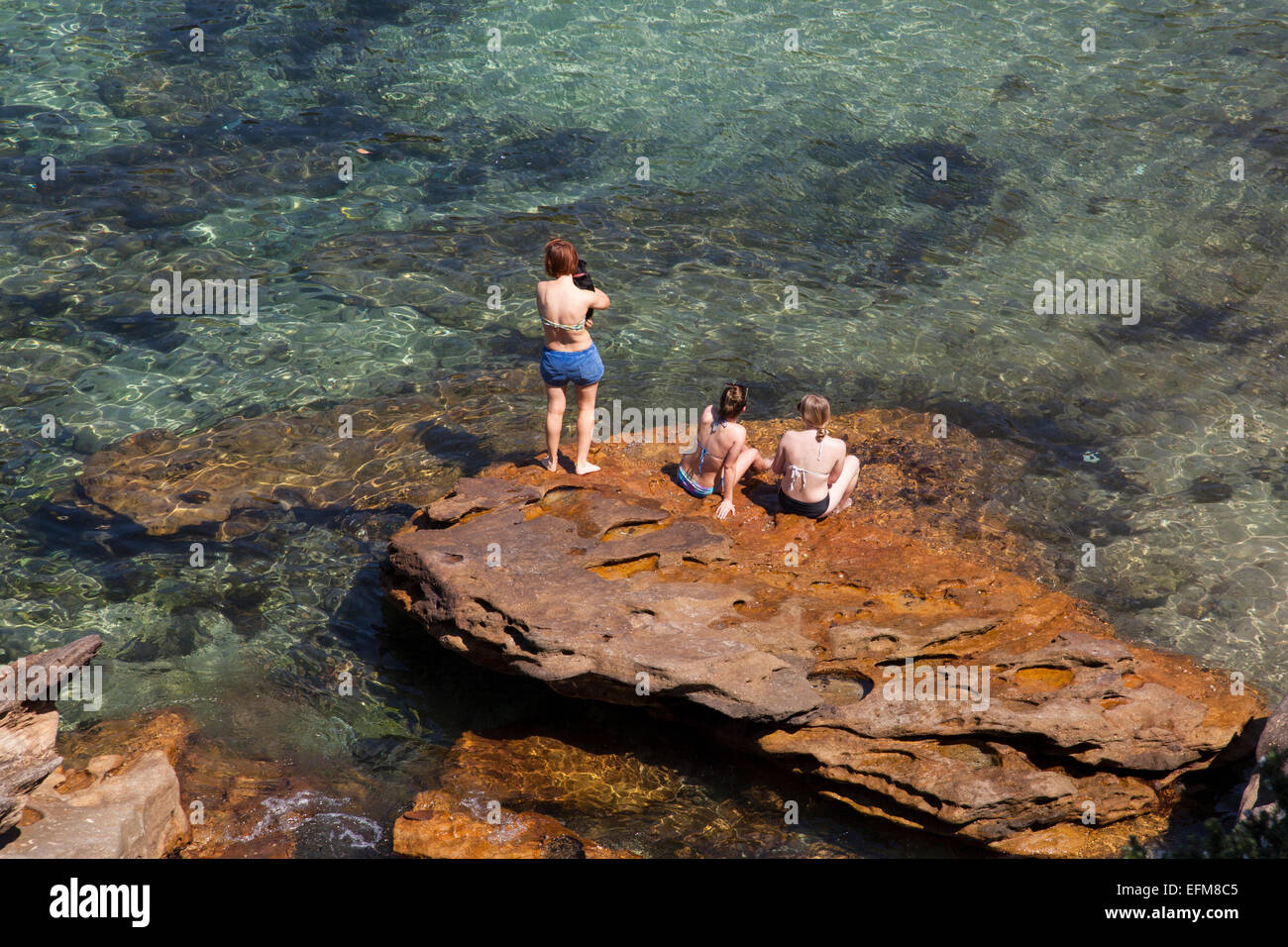 Frauen sitzen auf einem Felsen in Gordons Bay, Sydney, Australien Stockfoto