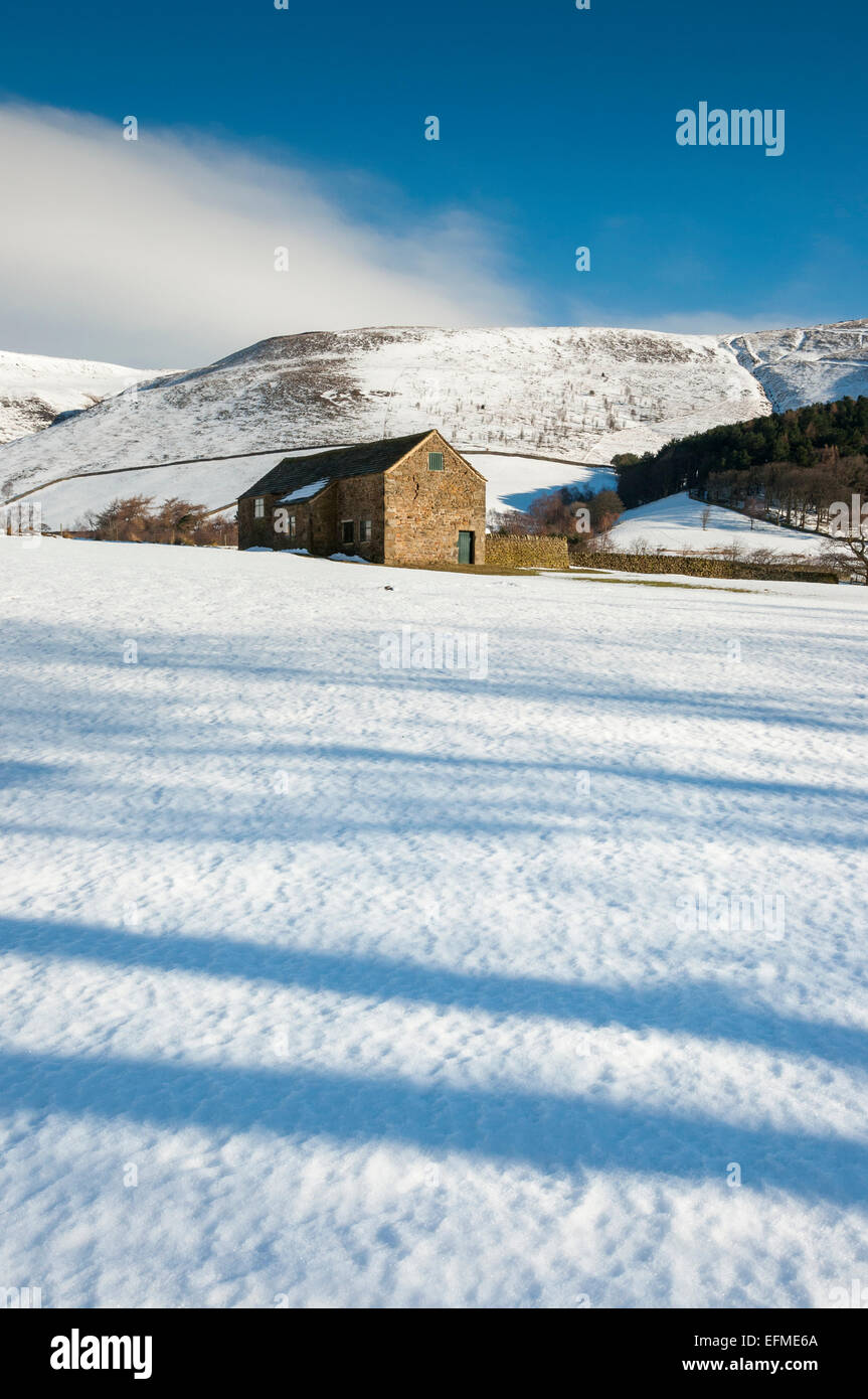 Eine Scheune in einer verschneiten Winterlandschaft im Tal von Edale, Peak District, Derbyshire. Schatten auf dem Schnee. Stockfoto