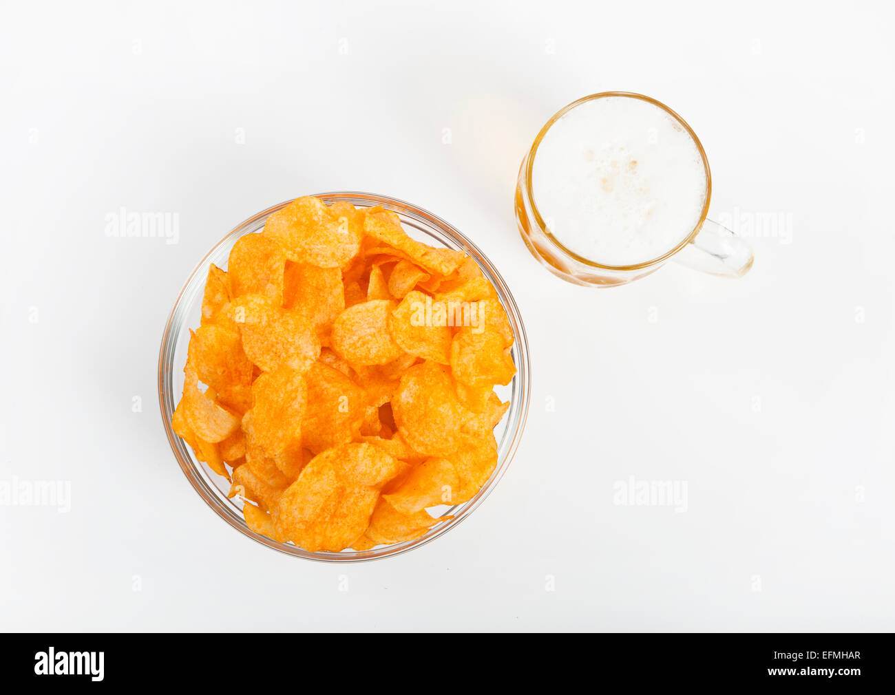 eine Glasschüssel gefüllt mit Kartoffel-Chips und ein Glas Bier vor weißem Hintergrund Stockfoto
