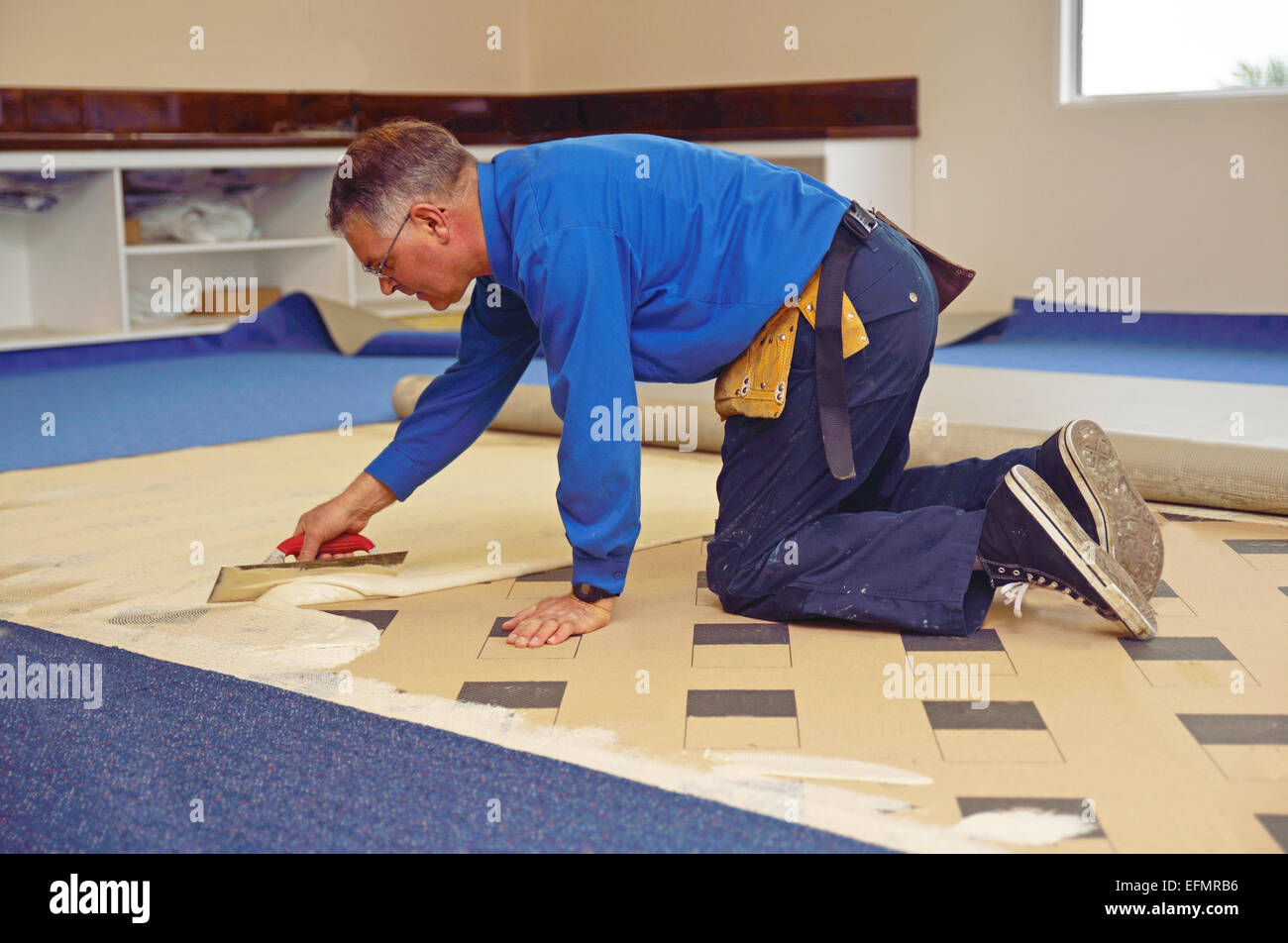 Ein Floorlayer breitet sich Klebstoff an der Unterlage für einen Teppich Verlegung job Stockfoto