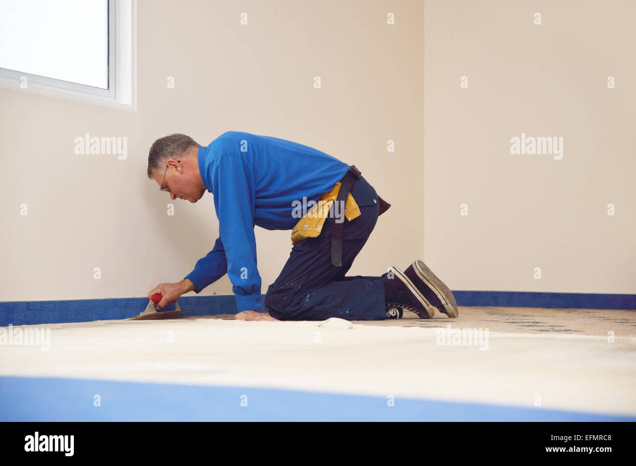 Ein Floorlayer breitet sich Klebstoff an der Unterlage für einen Teppich Verlegung job Stockfoto