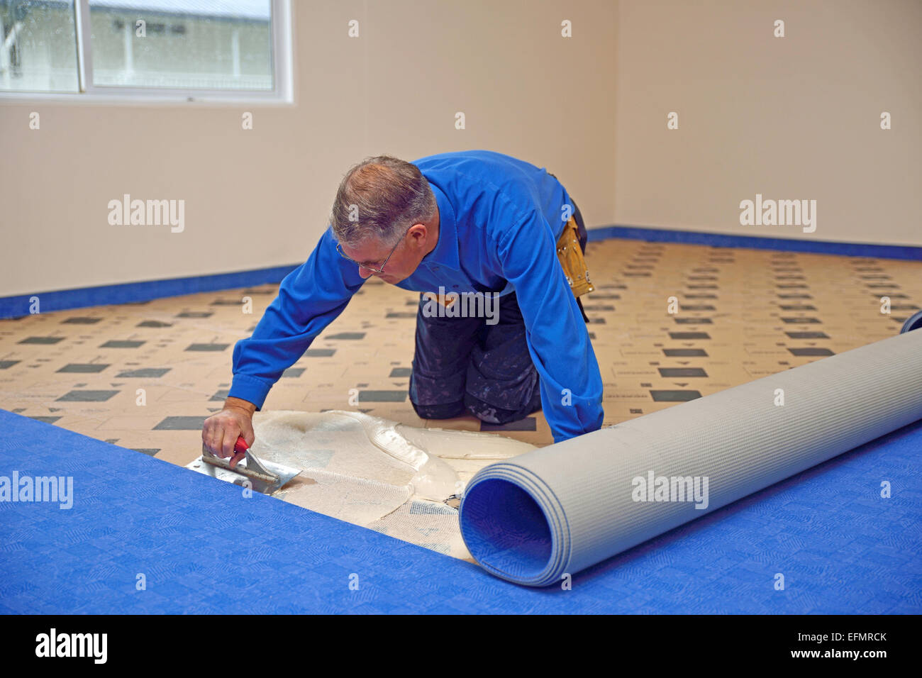 Eine Floorlayer verwendet eine Kelle, Kleber auf die Unterlage für einen Teppich Verlegung Job zu verbreiten Stockfoto