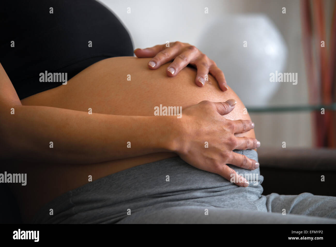Baby-Bauch, Bild 8 Monat schwangeren Frau sitzen auf einer Couch hält ihren Bauch Stockfoto