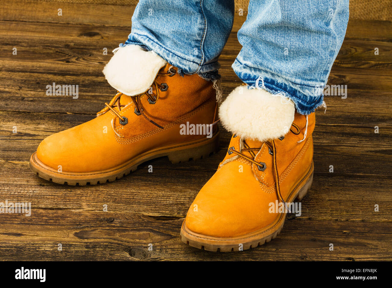 weibliche Füße im Winterstiefel und Jeans auf hölzernen Hintergrund Stockfoto