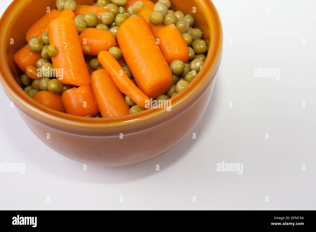 Gekochte Karotten und Erbsen auf rustikalen glasiertem Ton Schüssel. Isoliert auf weißem Hintergrund Stockfoto