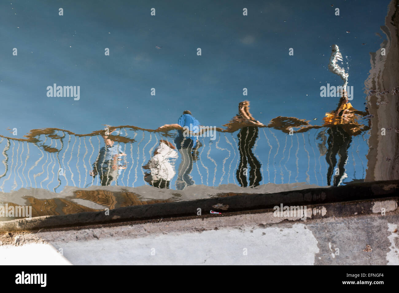 Verzerrten Reflexion über Wasser aus einer Gruppe von Menschen, die auf einem Geländer gelehnt. Stockfoto