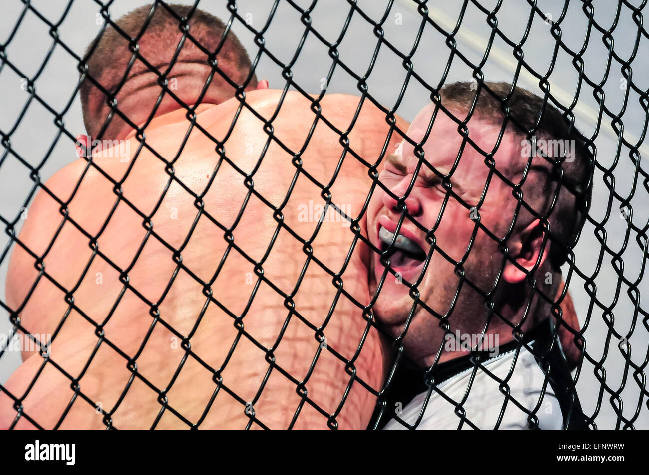 MMA-Kämpfer schreit vor Schmerzen nachdem er gefangen zwischen den Käfig und seinen Gegner, und sein Gegner hat ihn in eine Armlock. Stockfoto
