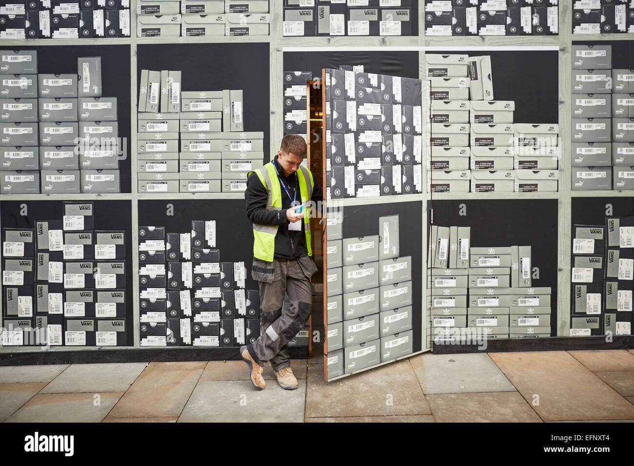 ein Arbeiter öffnet eine Geheimtür in den Betrieben für eine neue Größe-Schuh-Shop auf der Market Street Manchester UK Stockfoto