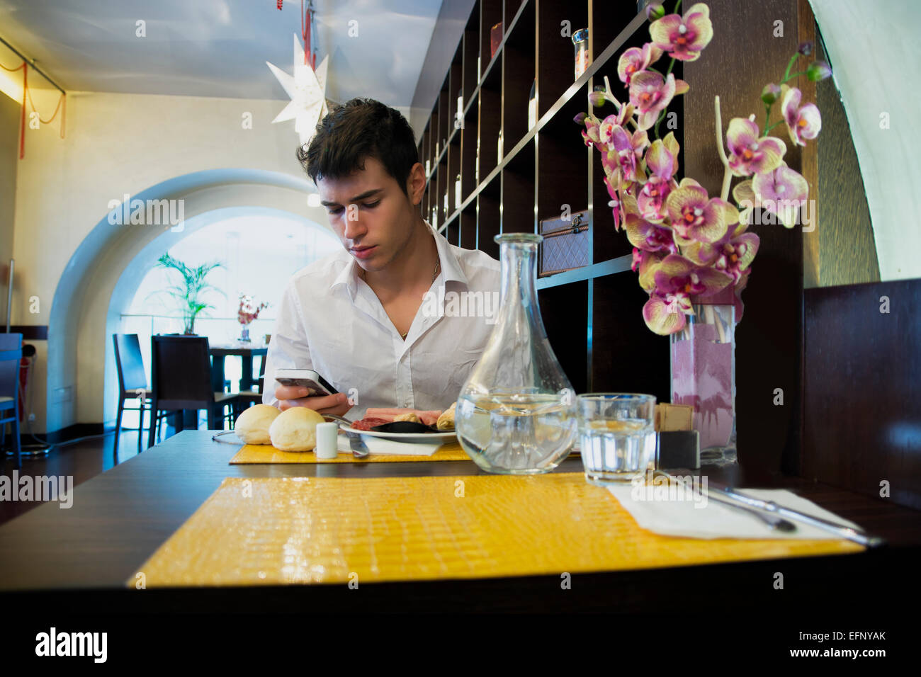 Hübscher junger Mann im eleganten Restaurant mit Handy Stockfoto