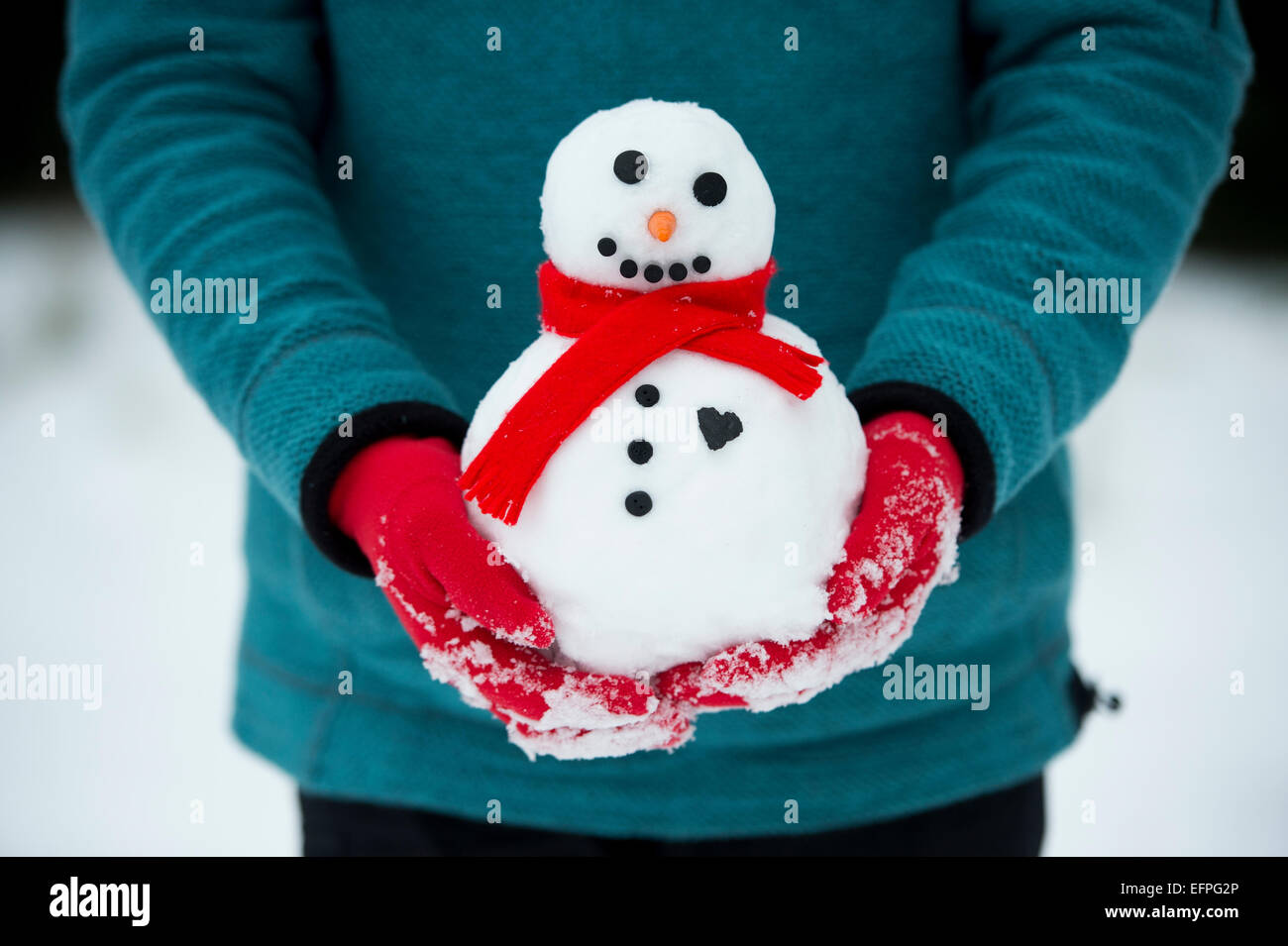 Rot behandschuhten Hände halten einen Schneemann mit einem großen Herzen Stockfoto