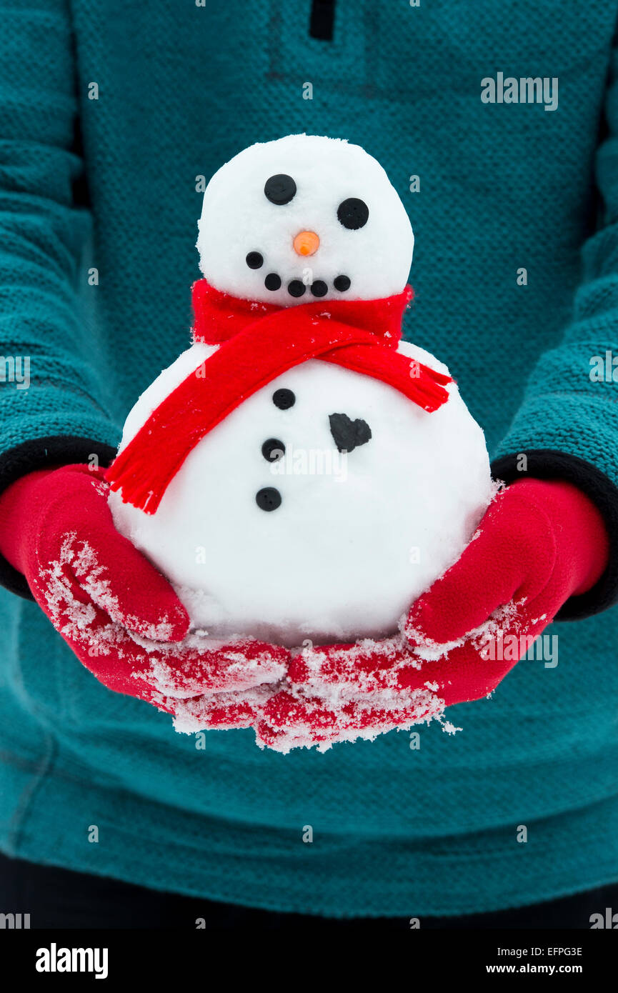Rot behandschuhten Hände halten einen Schneemann mit einem großen Herzen Stockfoto