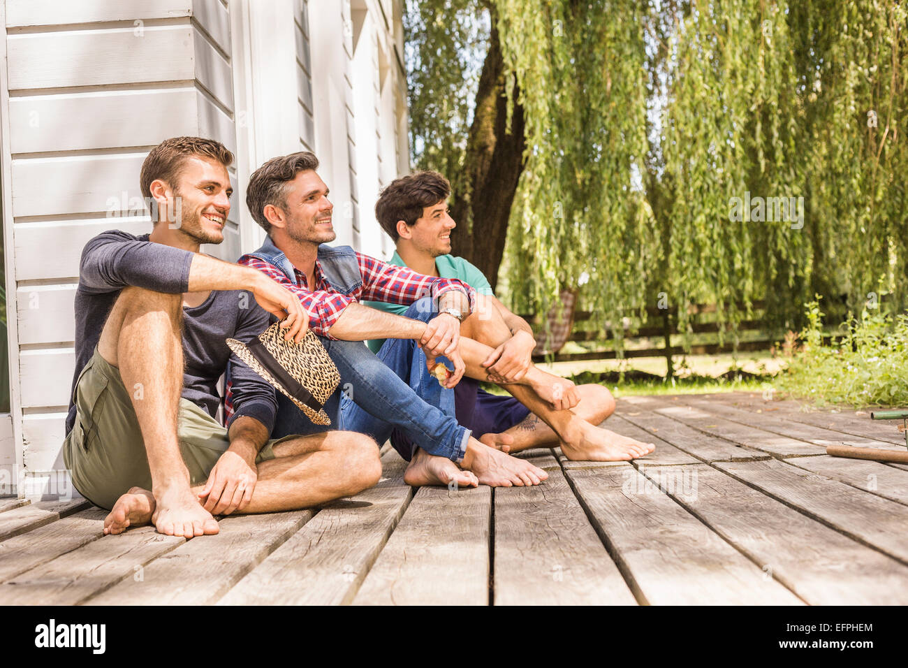 Drei Männer sitzen auf hölzernen Terrassendielen, wegschauen Stockfoto
