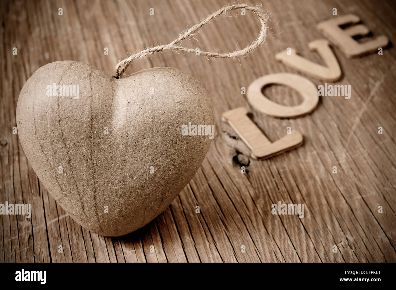 ein Karton Herz und Holz Buchstaben bilden das Wort Liebe auf einer rustikalen Holzoberfläche in Sepia Tönung Stockfoto