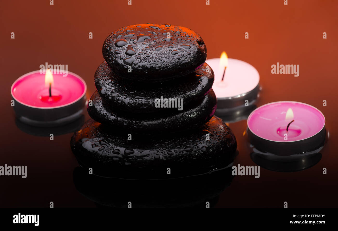 Massage-Steinen mit brennenden Kerzen und Wassertropfen Stockfoto