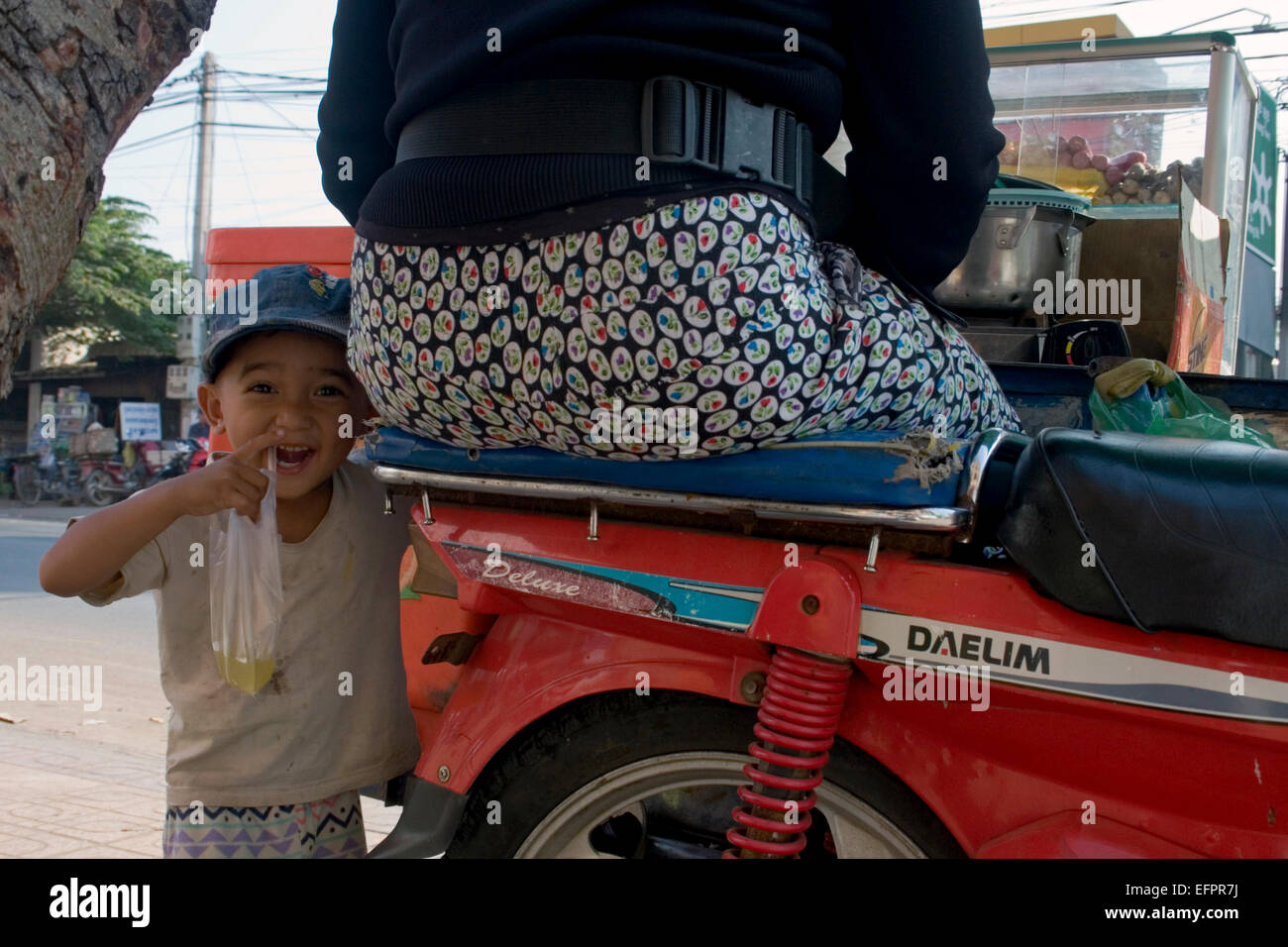 Ein kleiner Junge, der mit seiner Familie auf einem mobilen Straßenküchen Wagen reitet trinkt ein Zucker trinken in Kampong Cham, Kambodscha. Stockfoto