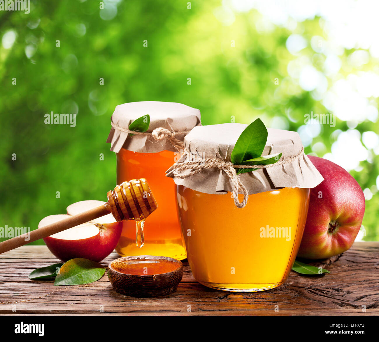 Glas-Dosen voller Honig und Äpfel auf alten Holztisch im Garten. Stockfoto