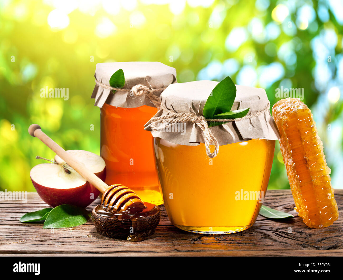 Glas-Dosen voller Honig, Äpfel und Kämme auf alten Holztisch im Garten. Stockfoto