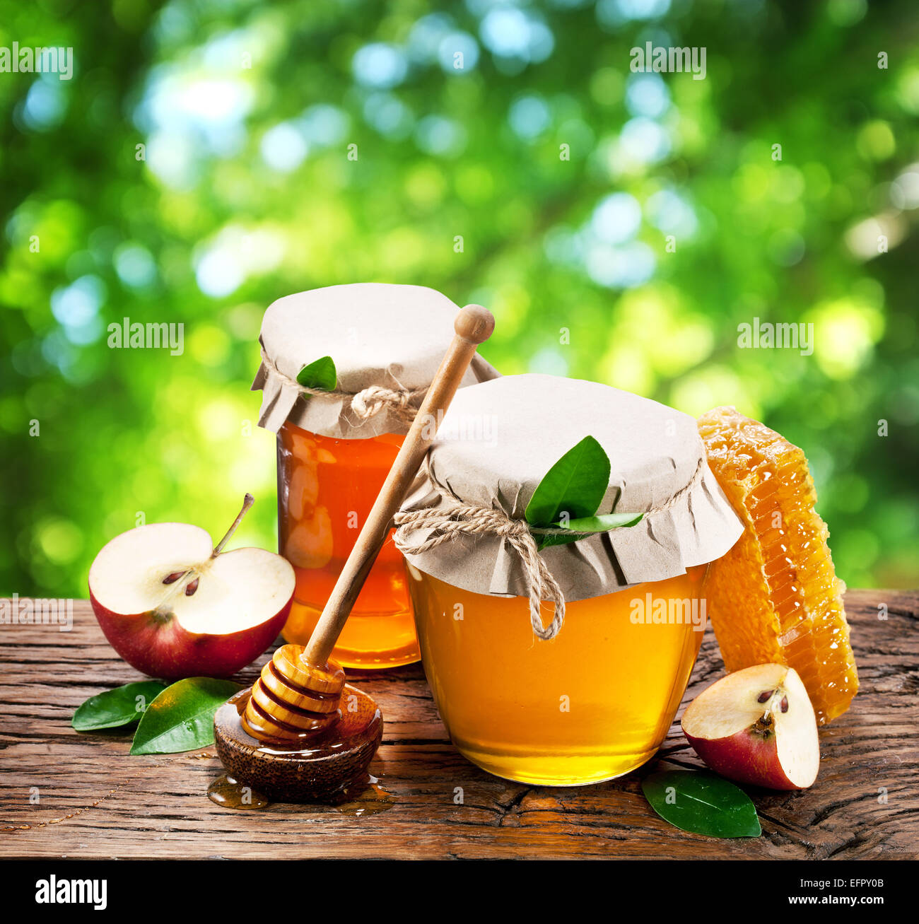 Glas-Dosen voller Honig und Äpfel auf alten Holztisch im Garten. Stockfoto