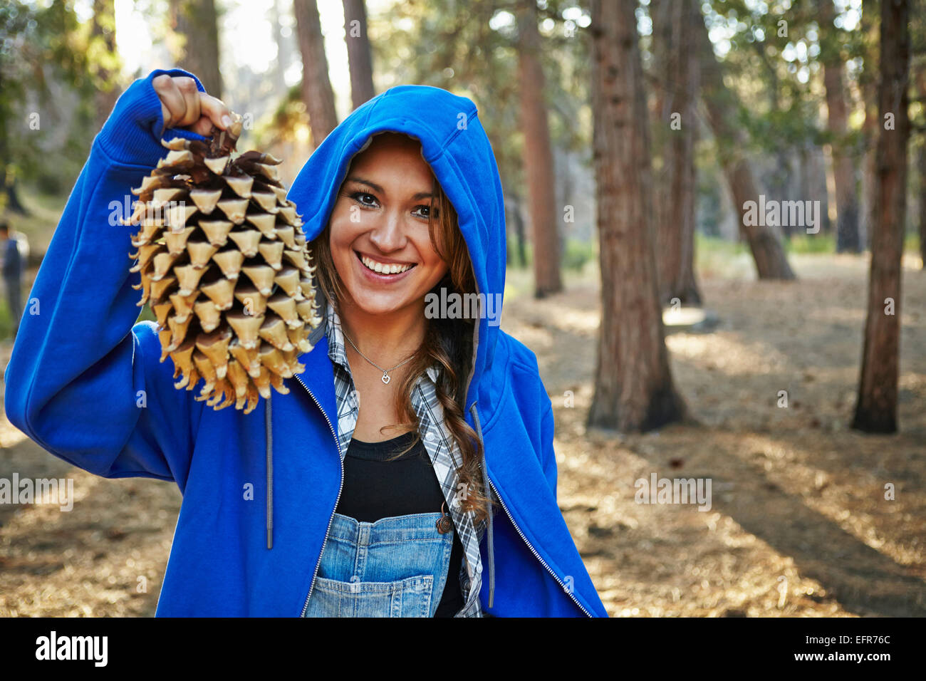 Porträt der jungen Frau im Wald hält große Tannenzapfen, Los Angeles, Kalifornien, USA Stockfoto